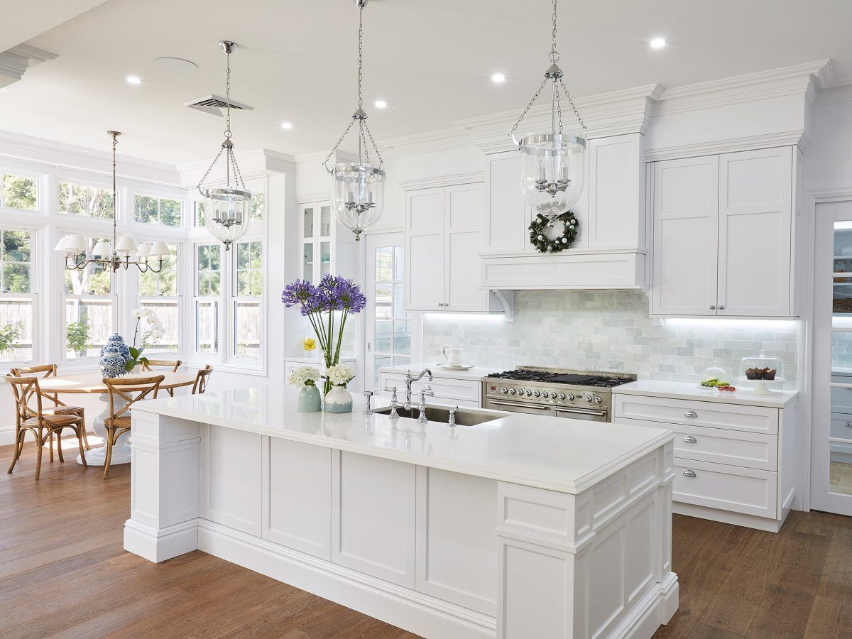 Bright white modern kitchen with marble island, pendant lights, and dining area by large windows