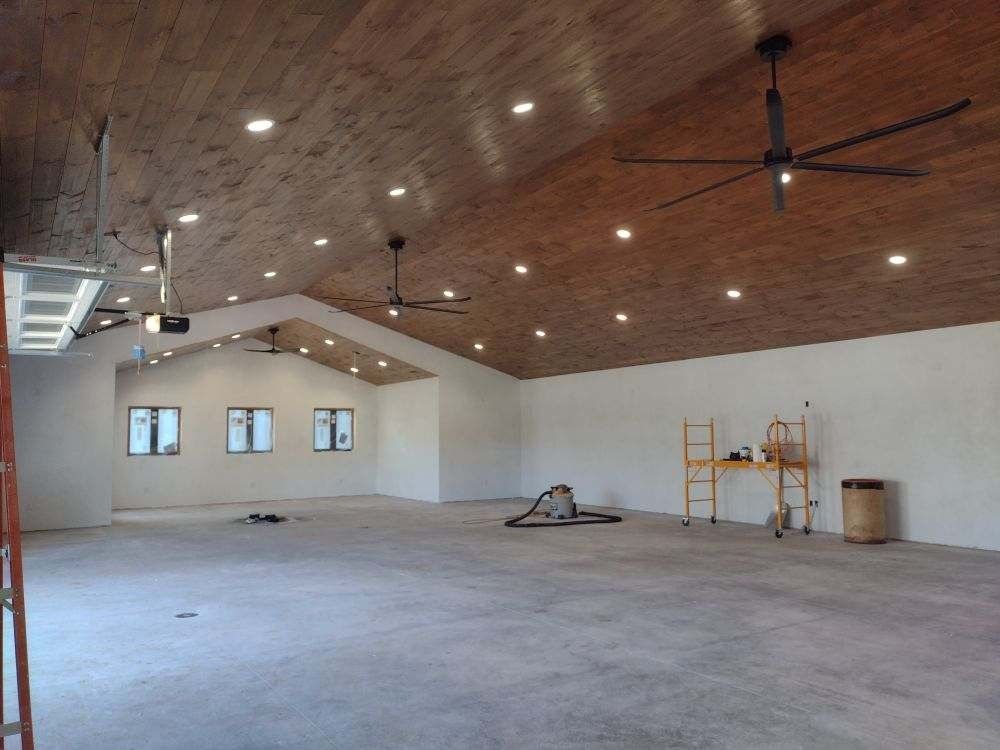 Large unfinished room with vaulted wood ceiling, ceiling fans, and scattered construction materials.