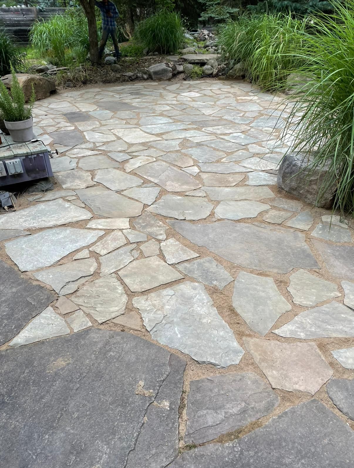 A stone patio made of irregularly shaped, light-colored flagstones set in a sand-filled garden landscape.