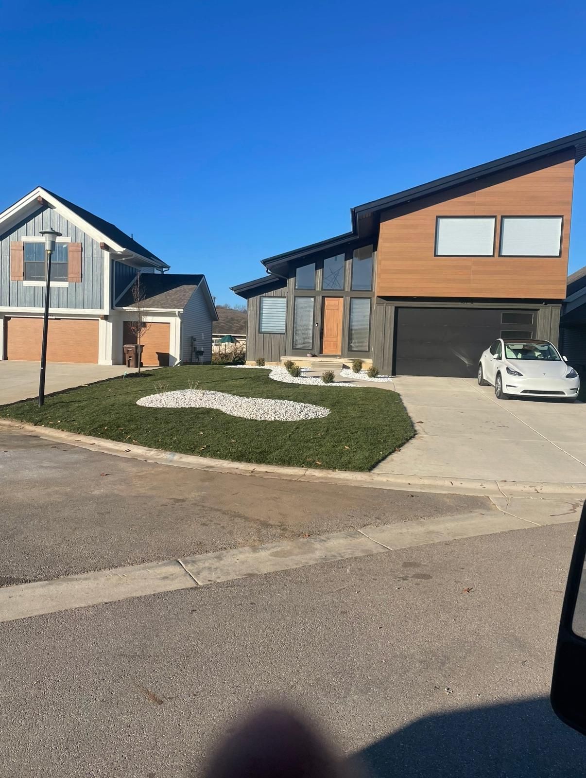 Two modern residential homes stand side-by-side on a sunny day with a white sedan parked in a concrete driveway.