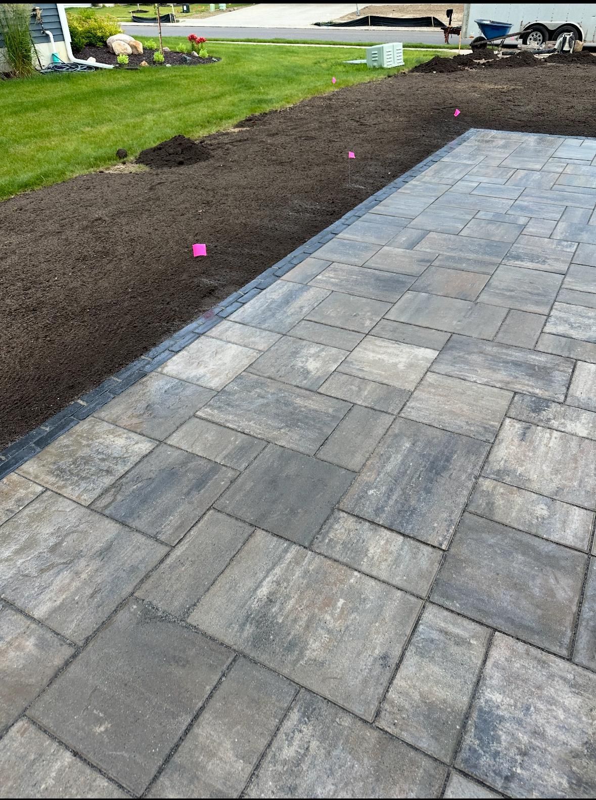 A paved stone patio with gray, rectangular blocks transitions to a patch of dark, freshly raked soil in a yard.