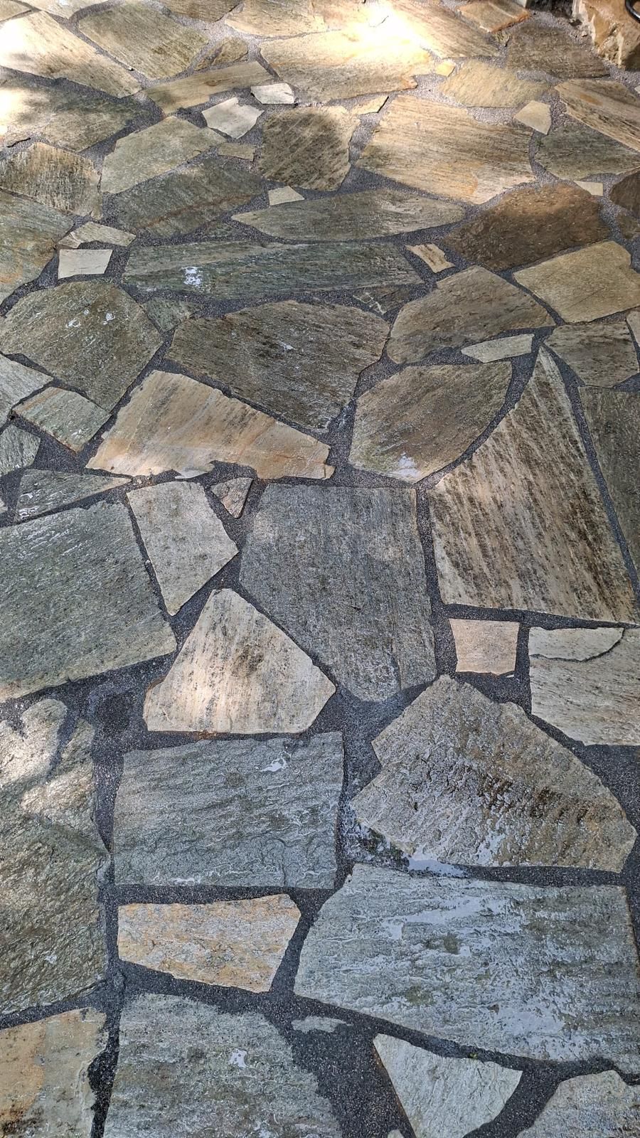 Flagstone patio floor made of uneven, grey and tan natural stones set in dark mortar.