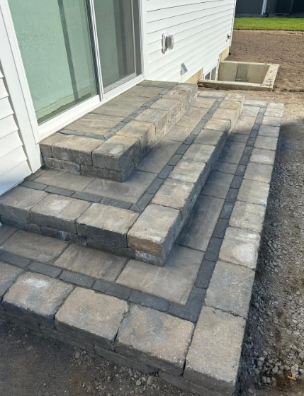 Stone block steps leading up to a sliding glass door of a white building, with a window well.