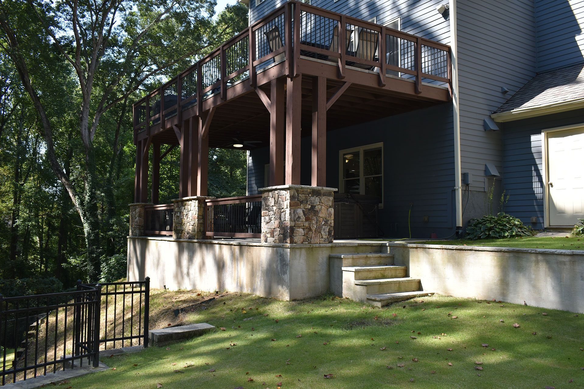 A raised wooden deck with stone-covered supports, stairs leading to the yard, and a house.