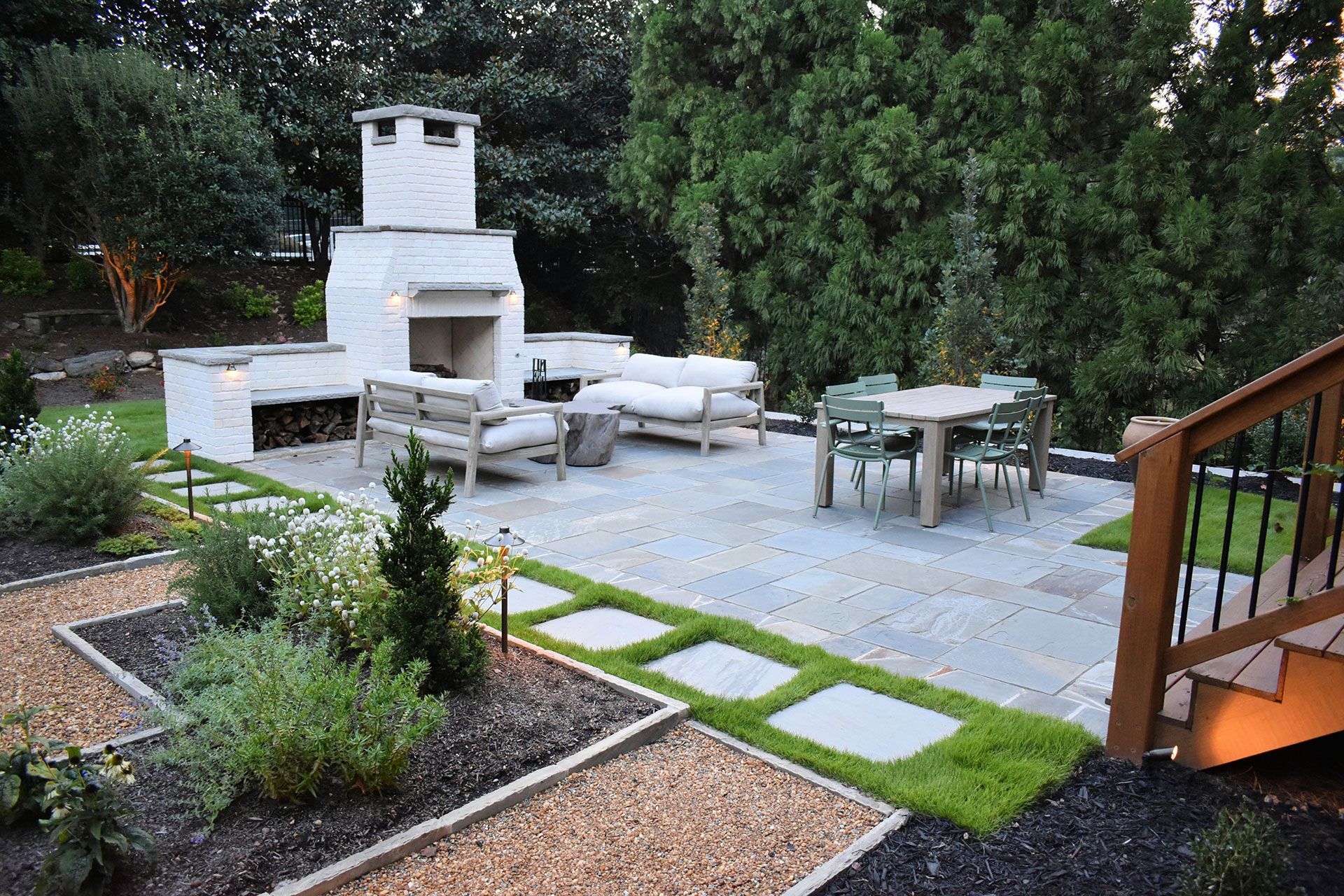 Backyard patio with fireplace, seating, dining table, and surrounding landscaping.