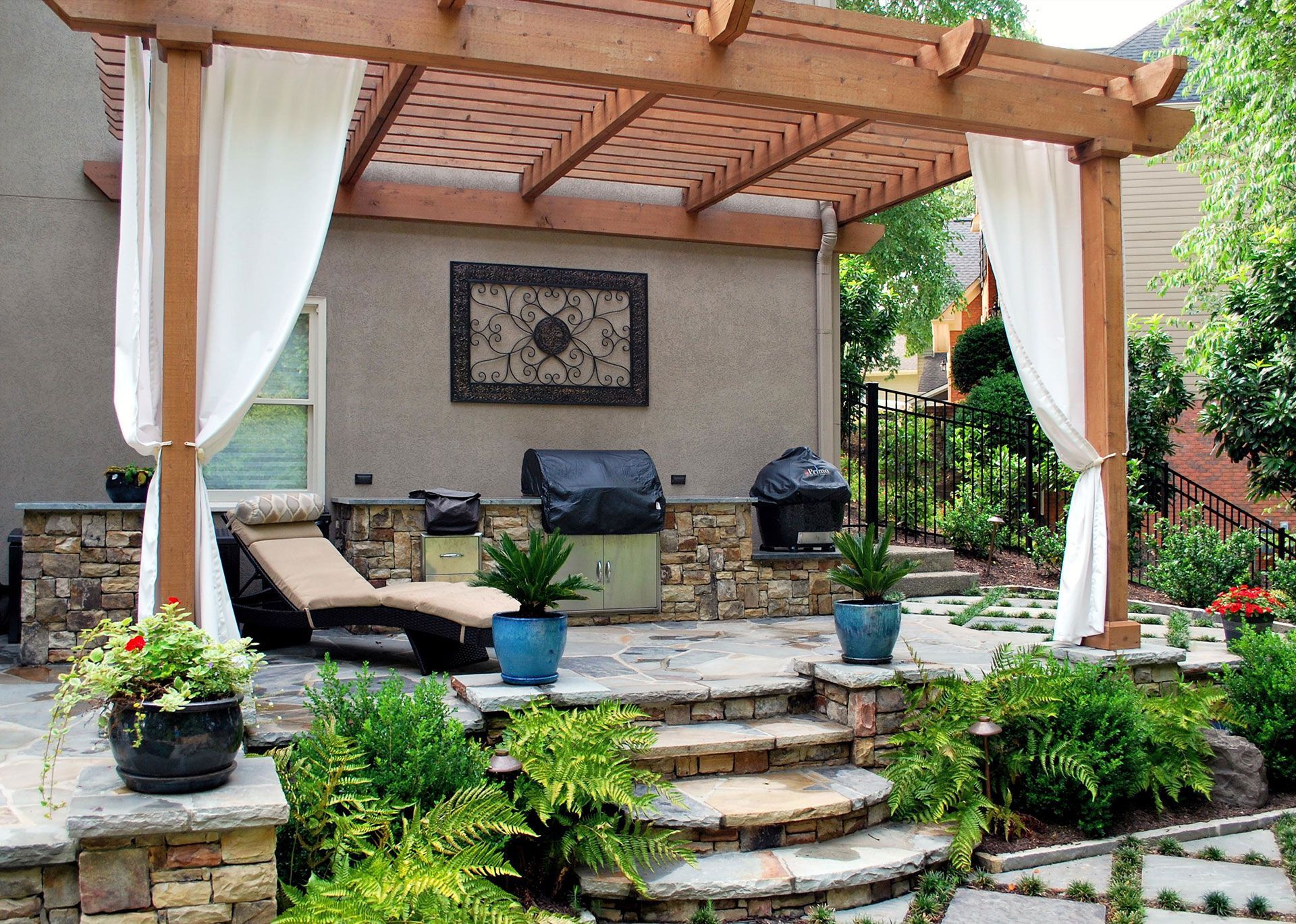 Outdoor patio with pergola, lounge chairs, grill, and potted plants, with white curtains.