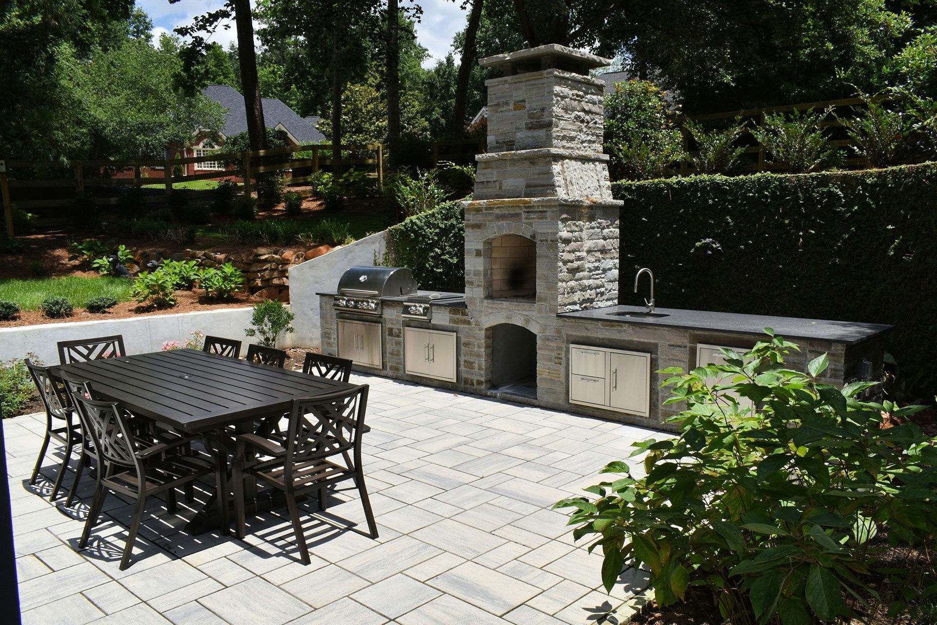 Outdoor kitchen with stone structure, grill, and dining table on a paved patio.