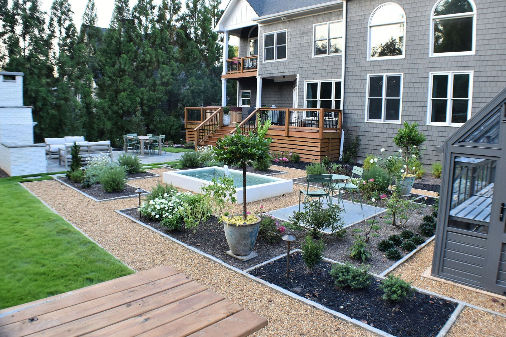 Backyard garden with gravel paths, raised beds, patio, and two-story house.