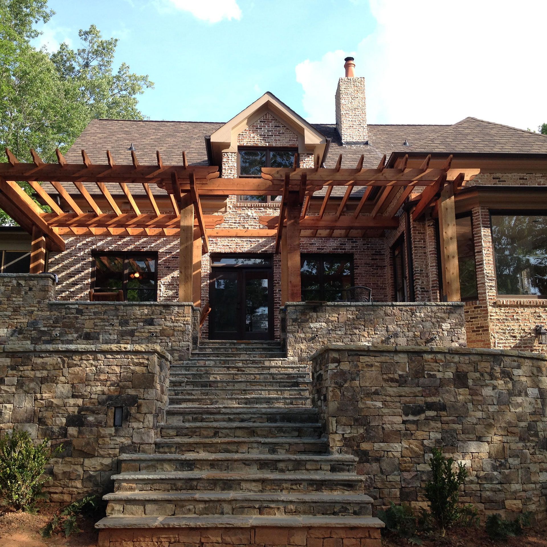 Stone house with pergola over a doorway and stone steps leading up to it.