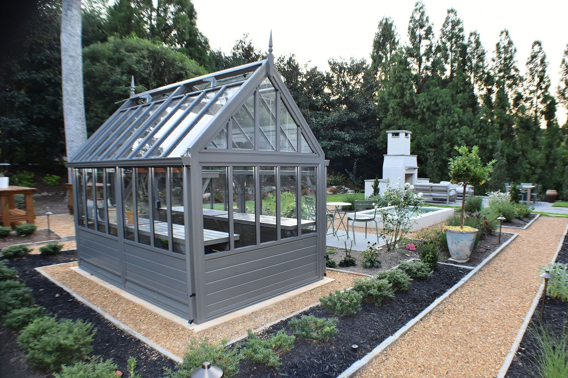 Greenhouse with angled roof in a garden setting, gravel path, and landscaping.