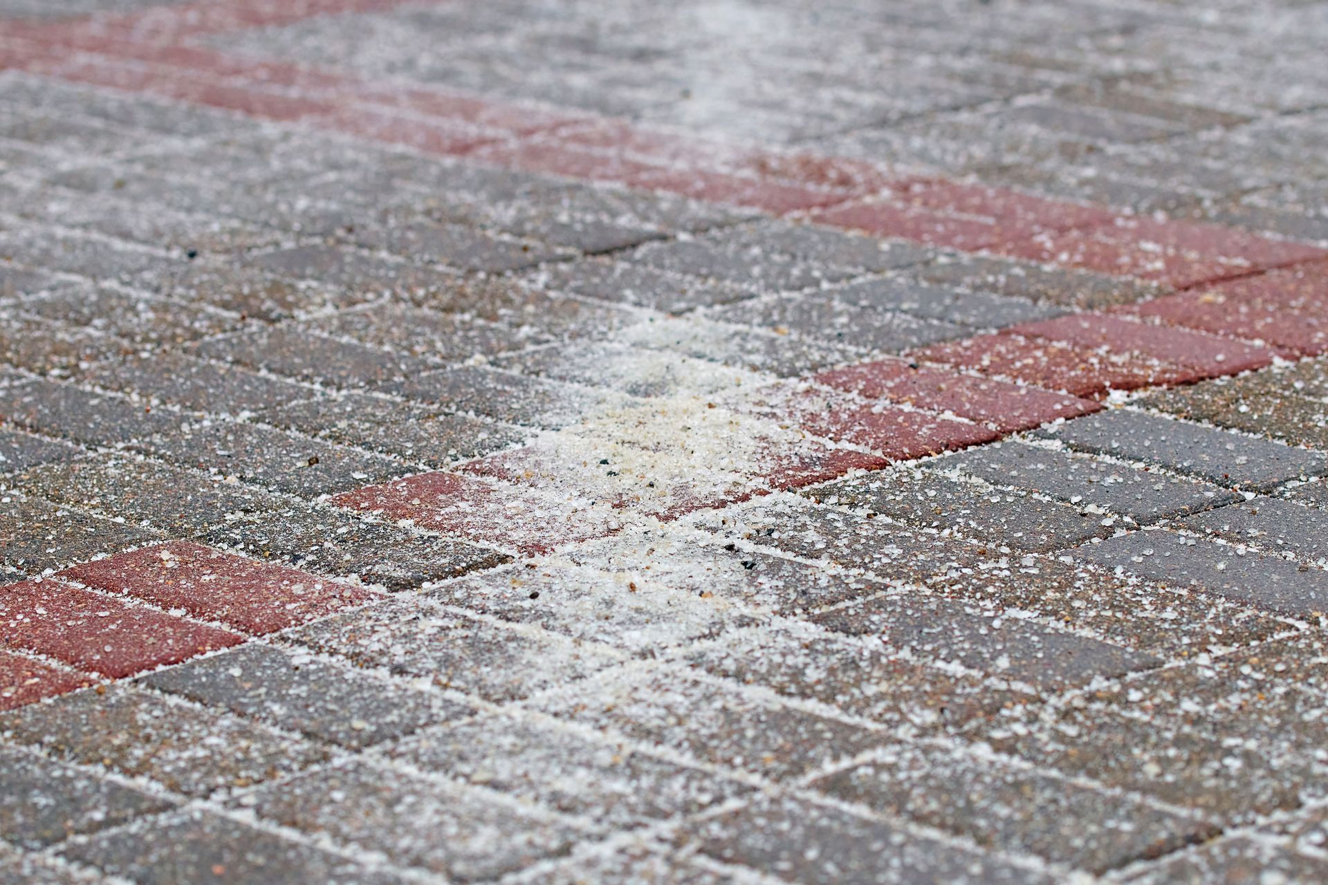 A pile of de-icing salt sprinkled over gray and red paved bricks during a light snowfall.