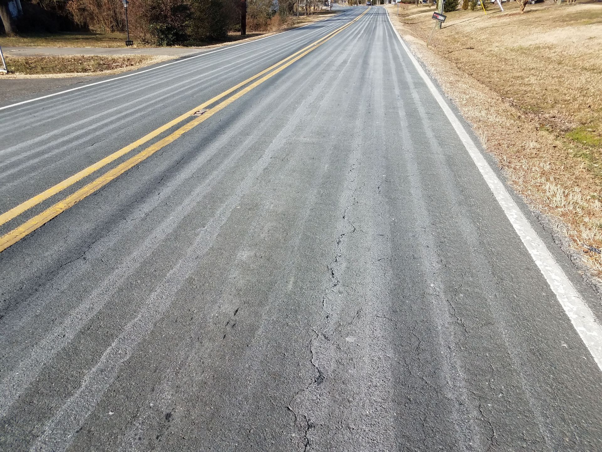 A two-lane asphalt road with yellow center lines and white edge lines, marked by repetitive streaks from road maintenance.