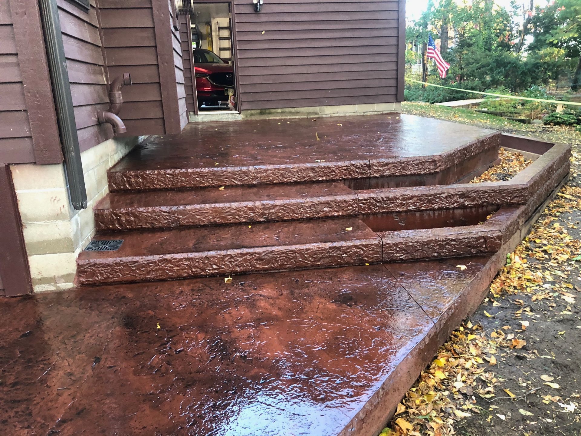 Stained concrete patio with textured steps leading to a house entrance, surrounded by fallen autumn leaves.