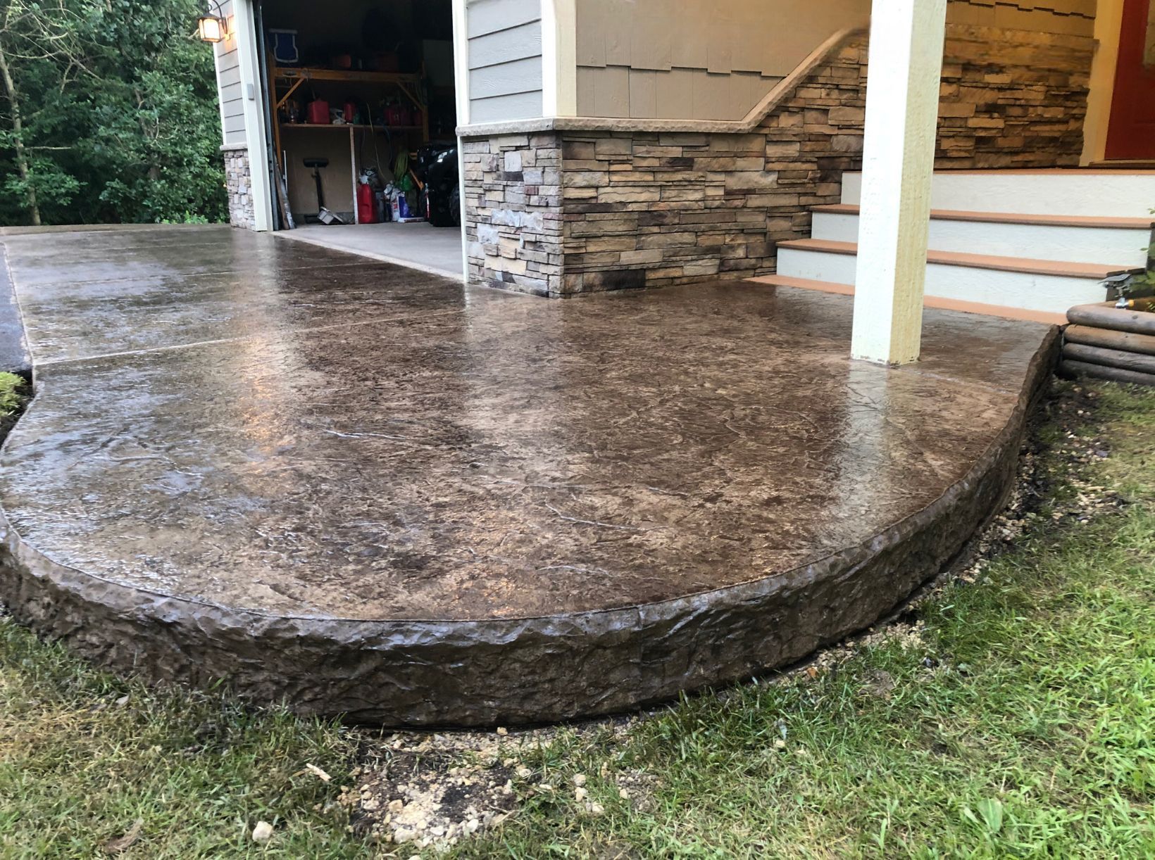A newly poured exposed aggregate concrete patio outside a brick house, bordered by wooden construction forms.