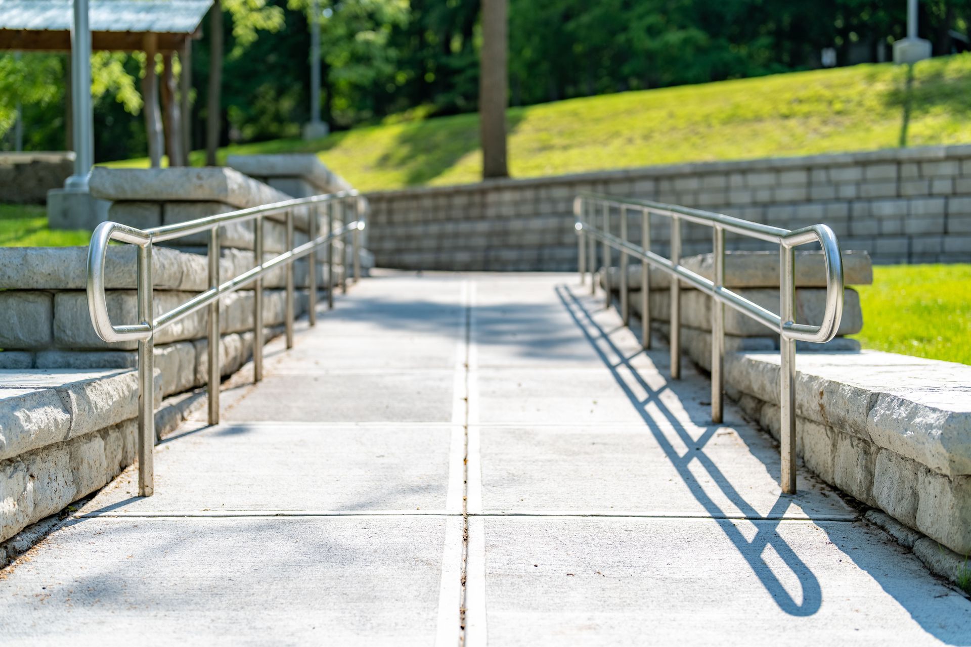 A paved accessibility ramp with metal handrails on both sides, set within a landscaped park area.