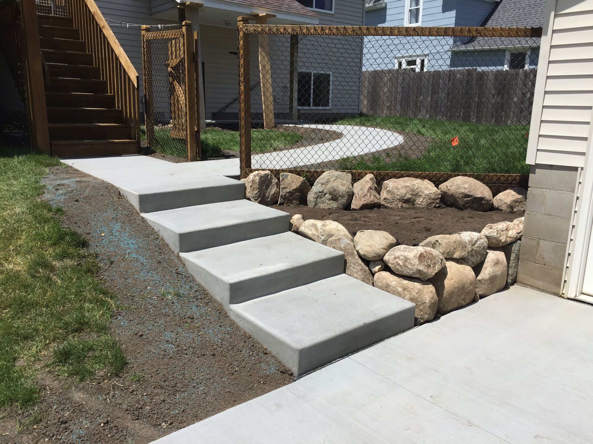 Concrete steps leading up from a driveway toward a house entrance, bordered by a decorative rock retaining wall.