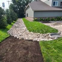 A dirt path going through a lush green lawn next to a house.