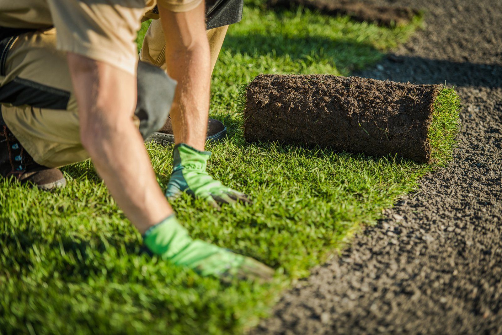 A man is kneeling down to roll out a roll of grass.