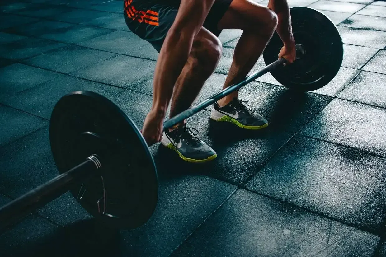 Man lifting a barbell with weights in a gym on a blue rubber floor.