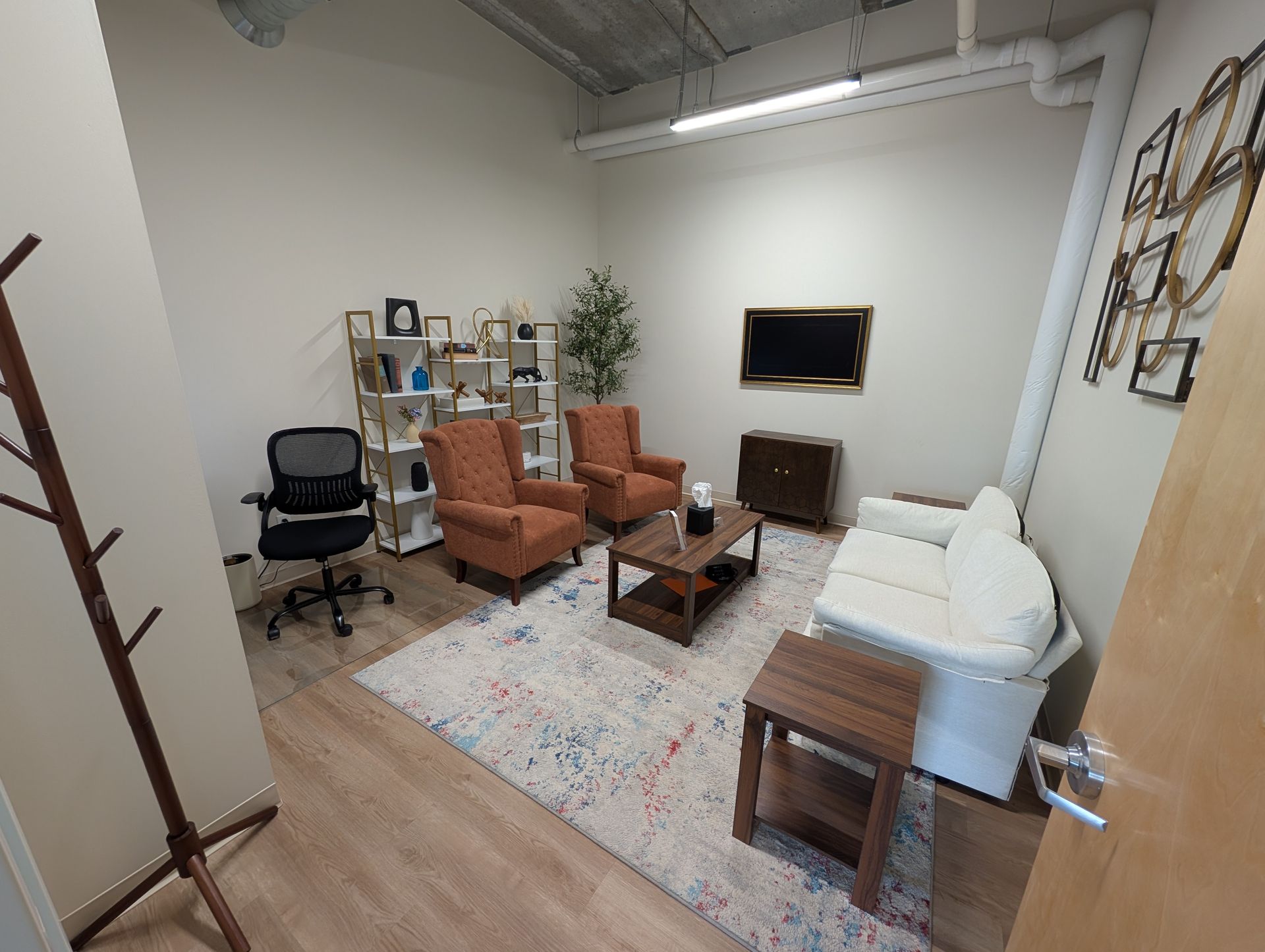 Therapy office: two orange armchairs, white sofa, wooden coffee table, and rug.