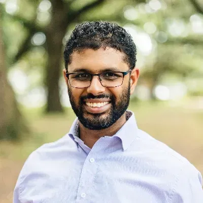 Man with glasses and a beard smiles at the camera, outdoors.