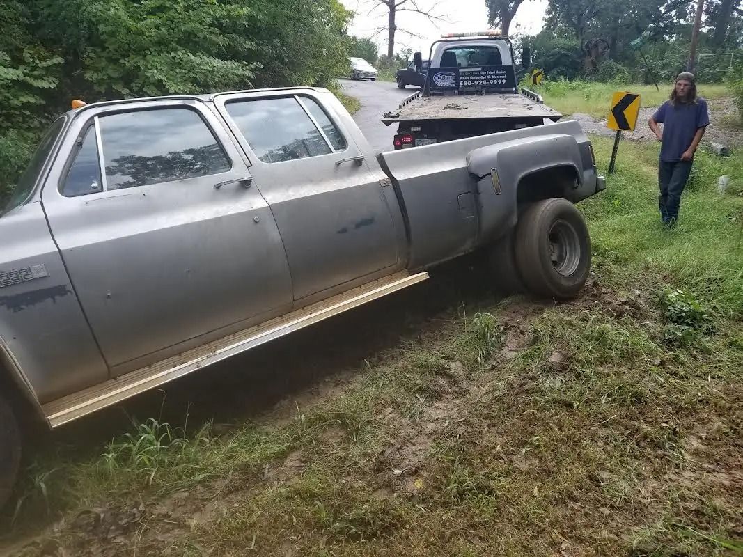 Silver pickup truck off the road, being towed. A man walks alongside the truck on a grassy shoulder.