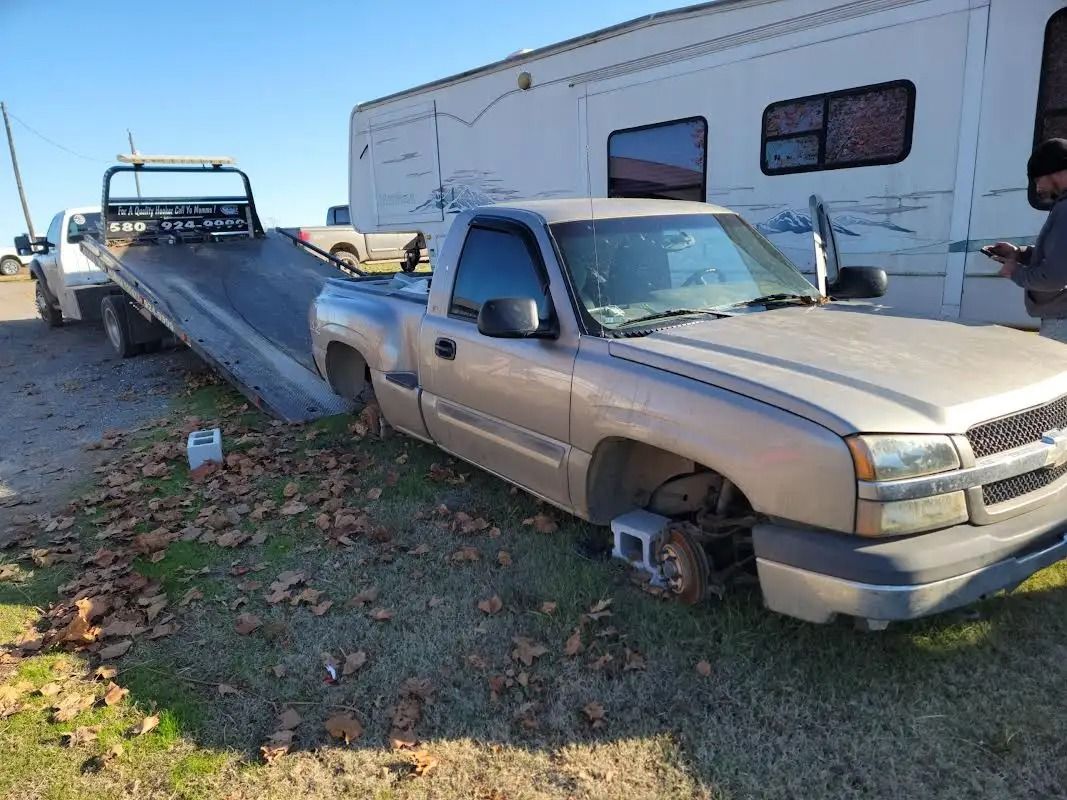 Silver pickup truck being loaded onto a tow truck, parked on grass near a camper.
