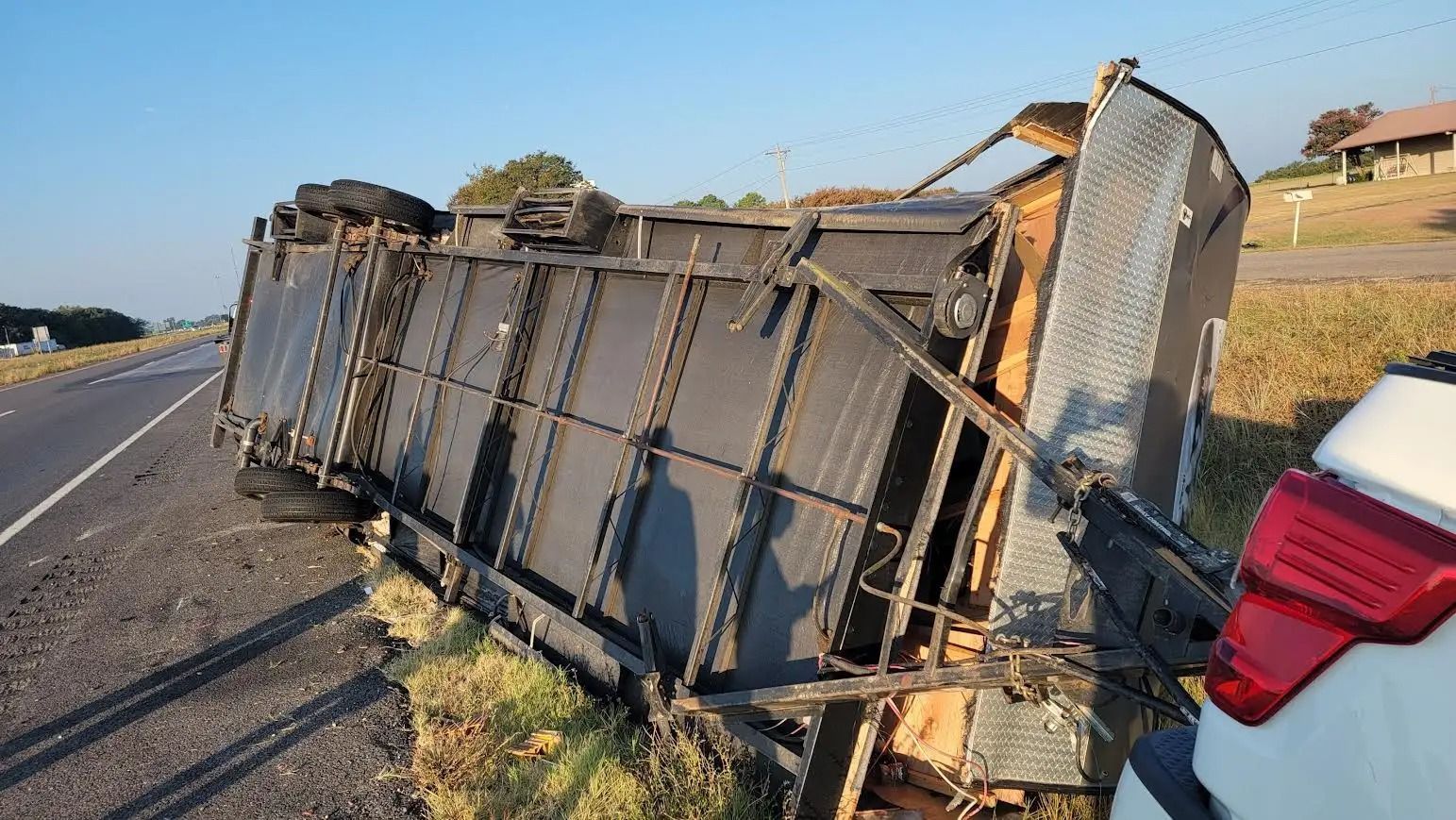 A large, black truck overturned on a roadside, next to a white car.