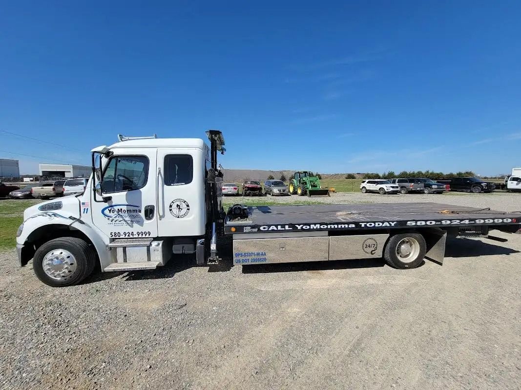 White flatbed tow truck on gravel under a blue sky.