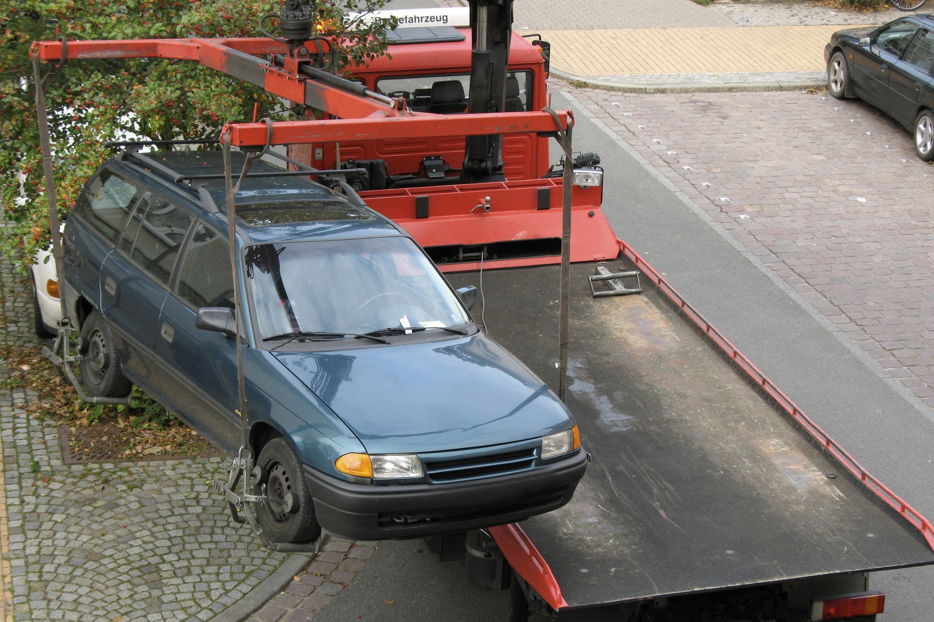 A blue station wagon being towed by a red tow truck on a city street.