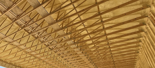 Wooden truss ceiling with repeating beams and diagonal supports in a warm tan interior