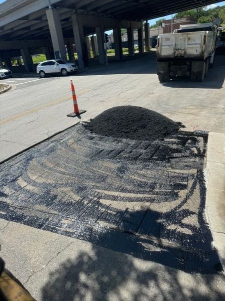 Asphalt patch on street under an overpass; pile of asphalt next to the patch; a truck in the background.