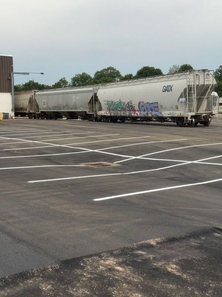 Train cars parked in an empty parking lot, some with graffiti. Cloudy sky.