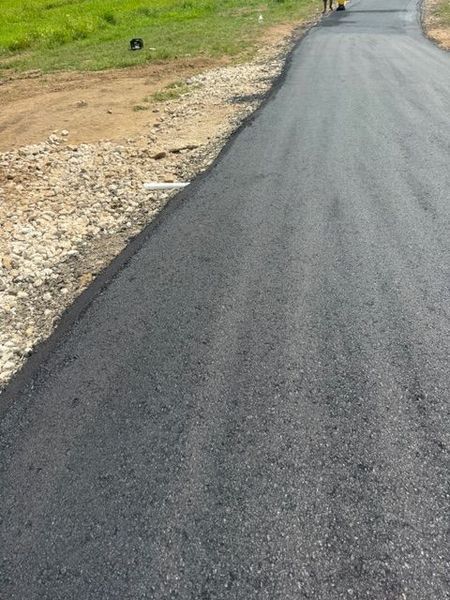 Newly paved asphalt road running through grassy and gravel terrain.