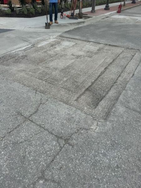 Man repairing damaged concrete in a public space; shovel, asphalt, cracked surface.
