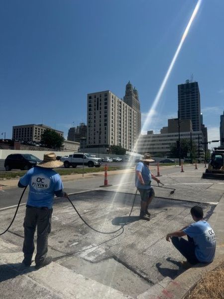 Three workers spraying a street in front of downtown buildings on a sunny day.