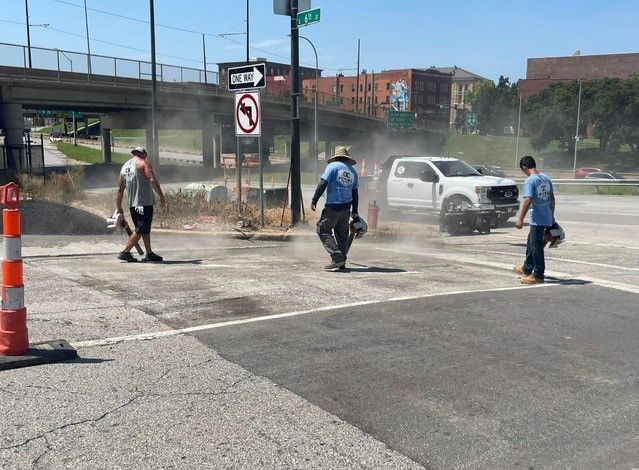 Dust cloud surrounds a white truck and three people on a city street corner.