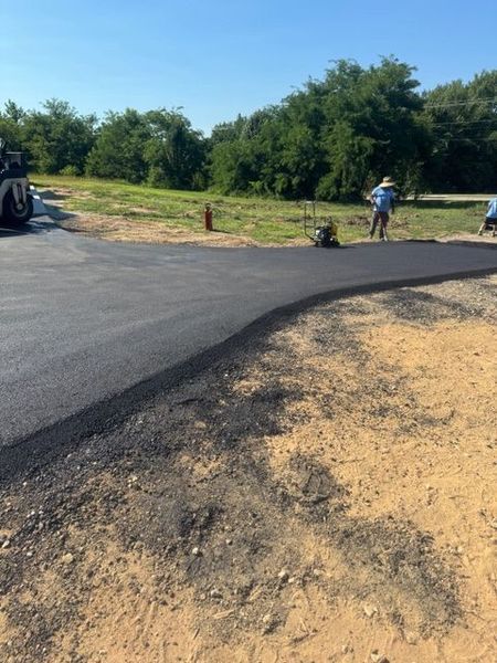 Newly paved asphalt driveway with workers and machinery, outdoors.