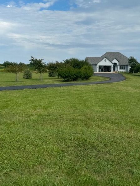 A house with a driveway on a grassy lawn under a cloudy sky.