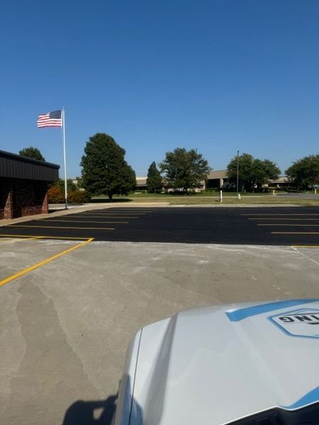 Paved parking lot with fresh asphalt, American flag, trees, building, and a white vehicle.