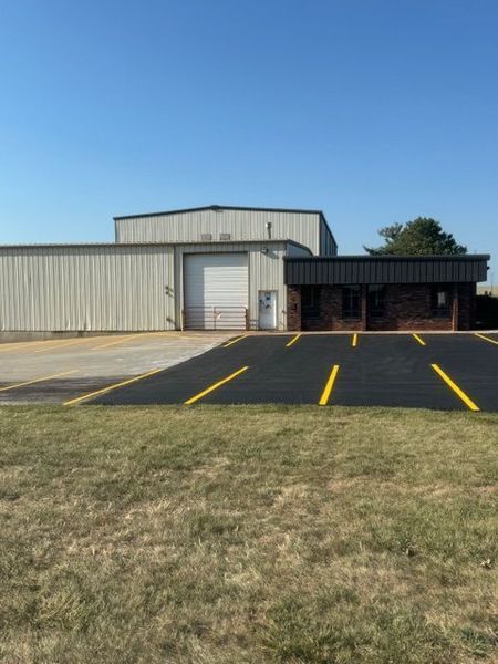 Building with loading dock and parking spaces; dark asphalt with yellow lines. Clear, sunny sky.
