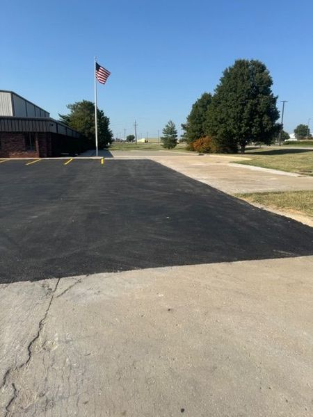 Black asphalt driveway with flag pole and building on a clear day.