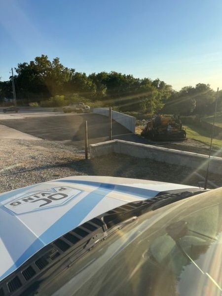 Bright sunshine over an outdoor area with a vehicle, retaining walls, trees, and sky.