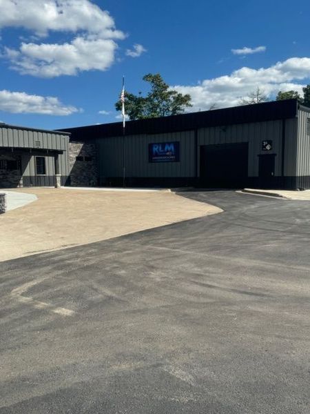 Building exterior with black facade, paved driveway, blue sign. Blue sky with clouds.