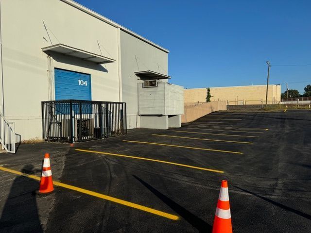 Warehouse loading dock with blue door and caged area, cones on asphalt parking lot.