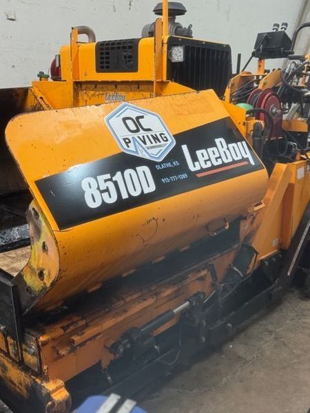 Yellow LeeBoy 8510D asphalt paver with OC Paving logo on the side, likely in a construction setting.