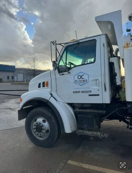 White OC Paving truck parked outdoors under a cloudy sky.