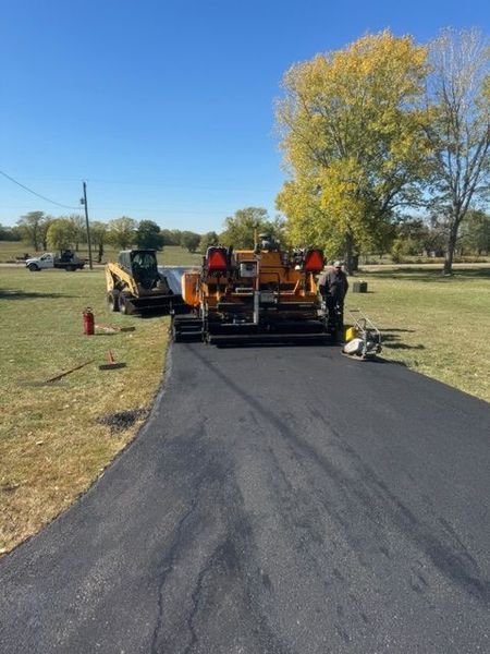 Asphalt paving in progress; paving machine laying fresh asphalt on a driveway.