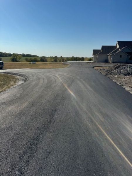 Asphalt driveway curves toward houses under a clear blue sky.