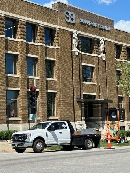 A white work truck parked in front of the Superior Bowen building, a brown brick structure with large SB logo.